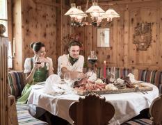 Blick in das Restaurant mit einer Brettljause am Tisch und 2 Gästen im Hotel Alpina