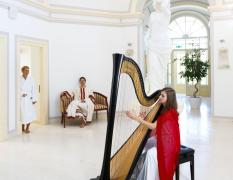 Eine Harfespielerin und zwei Gäste im Bademantel im historischen Teil des Wellnessbereiches im Rimske Terme Hotel Rimski dvor
